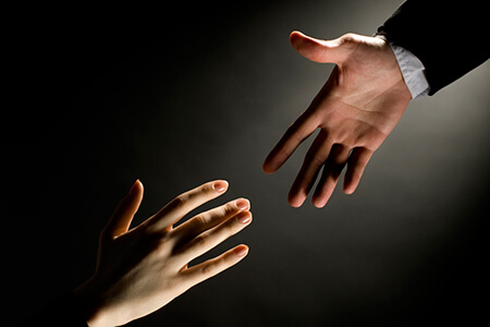 Męska dłoń wyciągnięta w kierunku kobiecej dłoni w geście pomocy